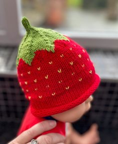 a knitted strawberry hat is being held by a doll's hand while wearing a ring