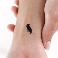 a small black bird tattoo on the wrist