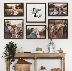 a table with pictures hanging on the wall next to a basket and vase filled with pumpkins