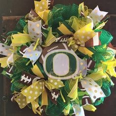 a wreath with a football on it that has green and yellow ribbons around the edges