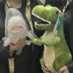 a person holding a stuffed toy dinosaur with its mouth open and teeth wide open, while another person holds a toothbrush in their hand