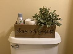 a wooden sign that says please seat yourself sitting on top of a toilet with a plant in it