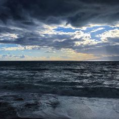 the sun is setting over the ocean with dark clouds in the sky and waves crashing on the beach