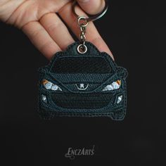 a hand holding a car shaped keychain in the shape of a small badge