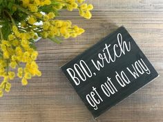 a wooden sign that says bol witch get out a way on it next to some yellow flowers