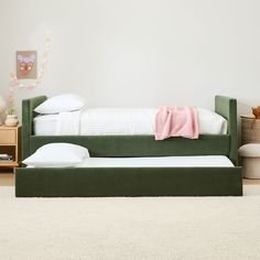 a green daybed with pillows and blankets on it in a white room next to a bed