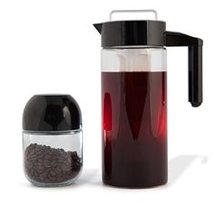 a glass pitcher filled with red liquid next to a container full of coffee beans on a white background