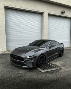 a black mustang parked in front of two garage doors with roller up doors behind it