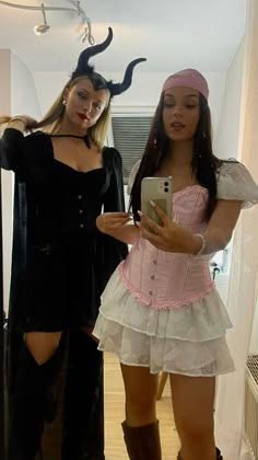 two women dressed in costumes standing next to each other and looking at a cell phone