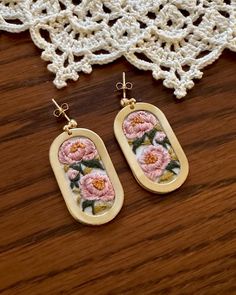 two earrings with pink flowers on them sitting on a table next to a doily