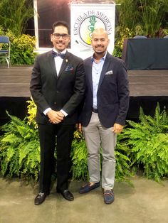 two men standing next to each other in front of plants