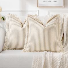 two pillows sitting on top of a white couch next to a vase with flowers in it