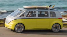 a small yellow van with surfboards on top driving down the road by the ocean