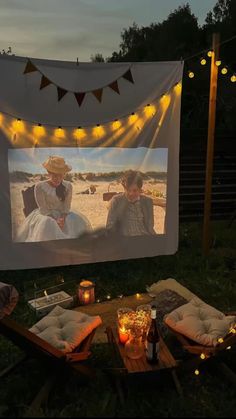 an outdoor movie screen with two people sitting on it and some candles in the grass