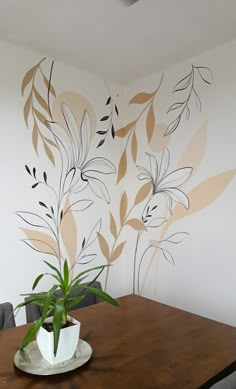 a wooden table topped with a potted plant next to a white wall painted with leaves