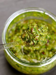 a spoon full of guacamole sitting on top of a glass jar filled with something