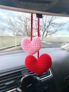 two crocheted hearts hanging from the dashboard of a car