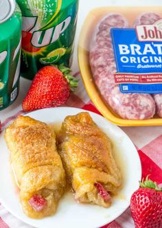 two pastries on a plate with strawberries next to cans of soda and fruit