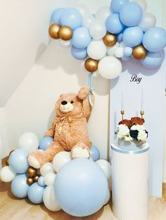 a teddy bear sitting on top of a table next to blue and white balloon decorations