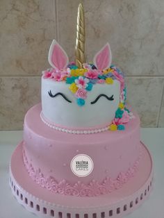 a pink cake with a unicorn face and flowers on it's top is sitting in front of a tile wall