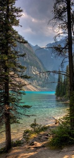 a lake surrounded by trees and mountains under a cloudy sky with sun shining on the water