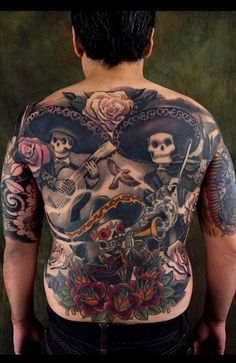 the back of a man with tattoos on his body and two skulls holding guitars in front of him