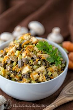 a white bowl filled with food next to some carrots and mushrooms on a table