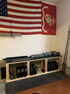 an empty gym with plates and dumbs in front of the american flag hanging on the wall