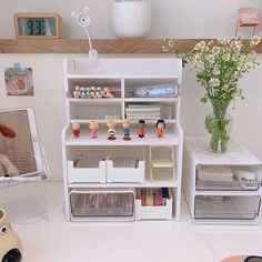 a white shelf filled with lots of toys next to a vase full of flowers and stuffed animals