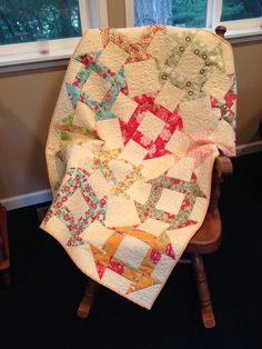 a chair with a quilt on it and a window in the back ground behind it