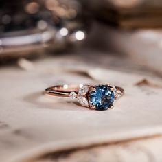 a blue and white diamond ring sitting on top of a piece of paper with other items in the background