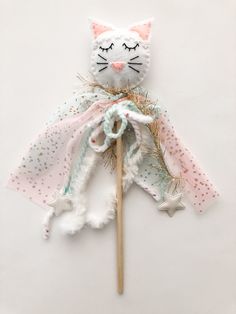 a white cat with pink and green decorations on it's head is holding a wooden stick