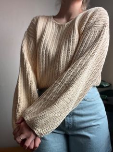 a woman is standing with her arms crossed in front of her face, wearing a sweater and jeans