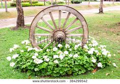 an old wooden wagon wheel surrounded by flowers and trees in a park with a sign that says