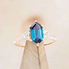 a ring with an emerald and diamond set in the middle, on top of a piece of wood