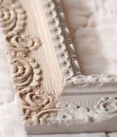 an ornate white frame sitting on top of a tablecloth covered table cloth with a bird perched on the edge