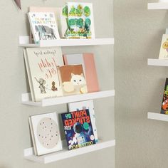 three white shelves with books on them in the corner next to a wall mounted book shelf