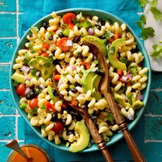 a bowl filled with macaroni salad next to two spoons and an orange juice