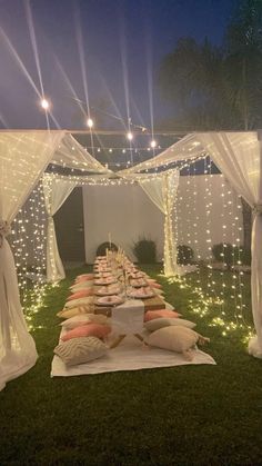 a long table covered in pillows and lights on top of a grass field at night