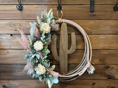 a wreath hanging on the side of a wooden wall next to two hooks with flowers