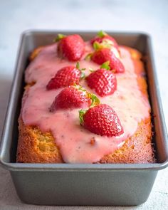 a loaf of strawberry bread in a pan with fresh strawberries on top and drizzled with icing