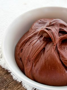 a white bowl filled with chocolate frosting on top of a wooden table next to a towel