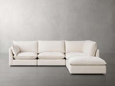 a white sectional couch sitting on top of a floor next to a chair and ottoman