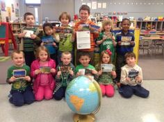 a group of children holding up their books in front of a globe with a map on it