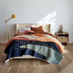 a bed sitting on top of a wooden floor next to a lamp and a white wall