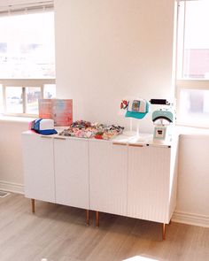 a white cabinet sitting in the middle of a living room next to a large window