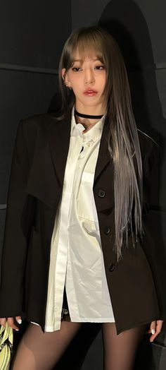 a woman with long hair wearing a white shirt and black blazer, standing in front of a wall