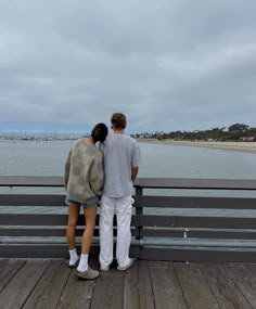 two people standing on a pier looking out at the water