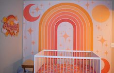 a baby crib in front of a wall with a rainbow mural on it's side