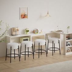 four stools in front of a white shelf with books and pictures on it, next to a plant